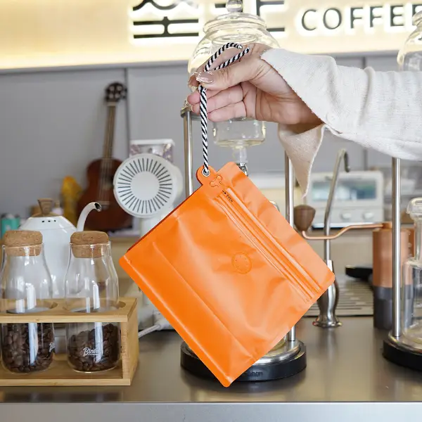 Sosteniendo de la mano bolsas de café de 250g con cordón en cafetería