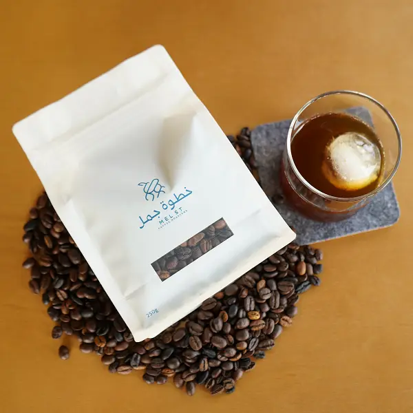 Colocación plana de la bolsa de café sobre granos de café tostados junto al café con hielo para la presentación del producto