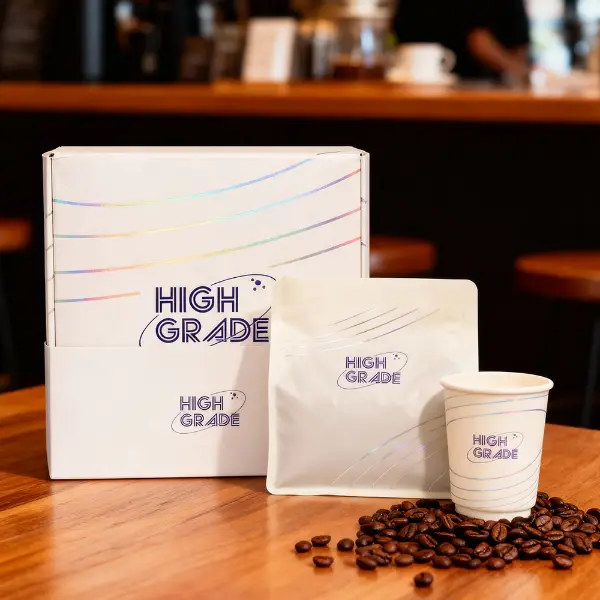 Caja de café personalizada de marca premium presentada con una bolsa y taza de café en un entorno de cafetería