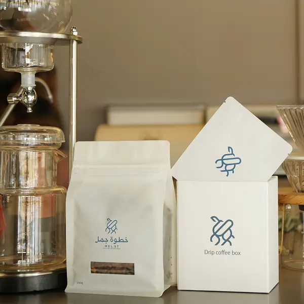 Caja de papel personalizada premium y bolsa de café exhibidas en un entorno de cafetería para exhibir la marca