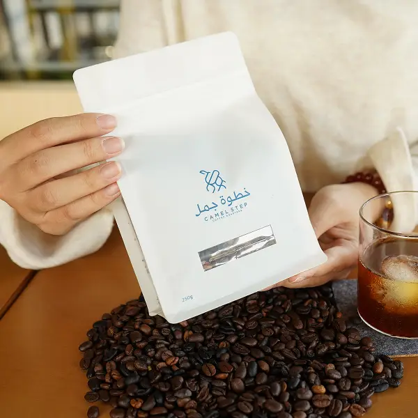 Cliente sosteniendo una bolsa de café blanca con una caja de papel impresa en un entorno de estilo de vida