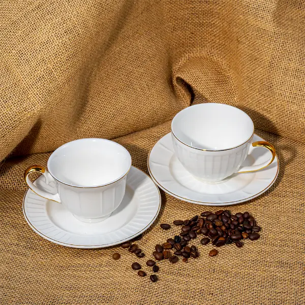 Taza personalizada de cerámica en relieve pintada en dorado con platillo expuesta con granos de café
