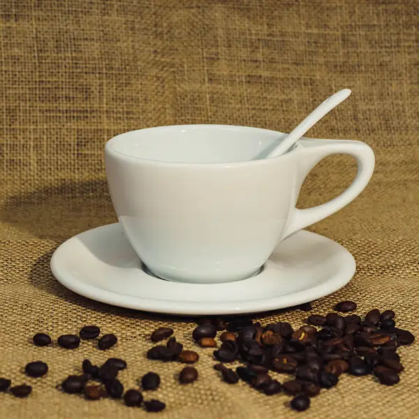 Taza de café cerámica blanca de tapa plana con asa expuesta y granos de café